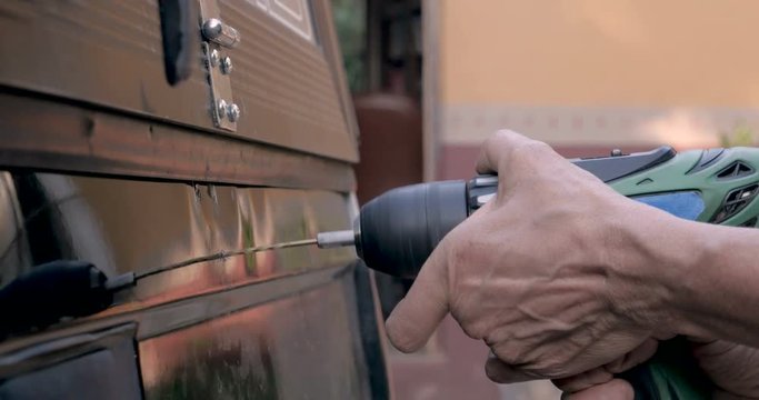 Close up of a hand holding a cordless drill drilling into the back of a truck