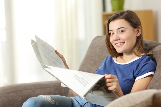 Teen reading a newspaper looking at camera at home