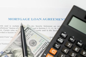 Mortgage loan agreement sign contract concept, pen on US dollar banknotes with calculator on mortgage form or contract, long term debt or real estate investment