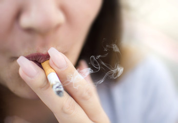 Close up of woman holding a cigarette in her hands smoking with smoke