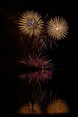 Fireworks of many colors on  display and refelcting in a lake