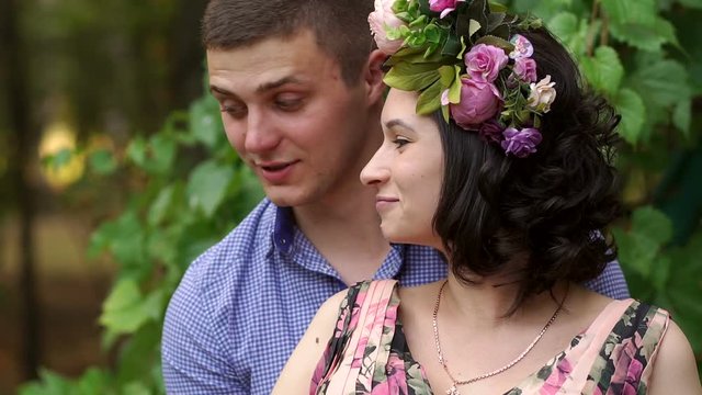 Husband tenderly hugging pregnant wife. A pregnant woman in a beautiful dress with flowers in the Park with her husband, she has a wreath of bright flowers on her head.