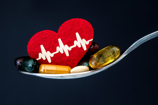 the colorful medical supplement and drug pills with red heart in spoon , pharmaceutical cardiology drugs for heart health care disease concept