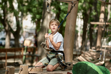 Exhausted little boy climbing at treetop adventure park