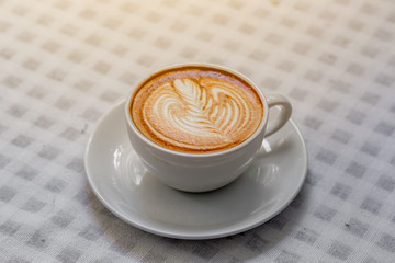 The hot coffee art in the white ceramic mug in the restaurant or coffee shop on white table cloth. 
