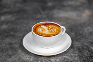 The hot coffee art in the white ceramic mug in the restaurant or coffee shop on dark marble surface. 