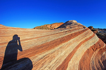 Fototapeta na wymiar Photographer sitting on the Fire Wave rock at sunset, Valley of Fire State Park, Nevada, USA