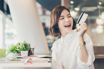 Young beautiful asian woman working on desk with tablet and showing credit card in coworking spaces.