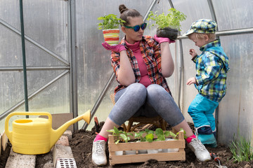 Charming peasant woman with son is posing in greenhouse with vegetable seedlings. Box with fresh...