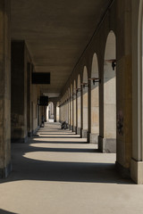 Arcades with shadows of columns on the pavement - covered walkway enclosed by a line of arches outside the building on a sunny day. House Without Edges by Czeslaw Przybylski built in 1935 in Warsaw.