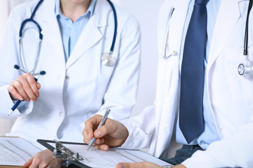 Two unknown doctors filling up medical form on clipboard, just hands closeup. Physicians asking question to patient or discussing medication program. Healthcare, insurance and medicine concept