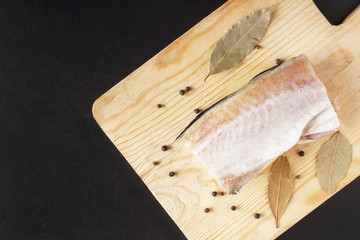 Meat pollock with spice closeup. Pepper peas and bay leaf for dish from seafood. Top view on black background. Copy space
