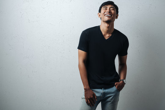 Cheerful asian guy in black blank t-shirt, grunge wall, studio portrait