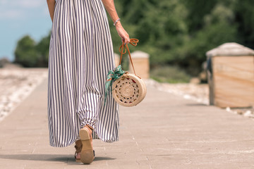 Woman with fashionable stylish rattan bag nude color and silk scarf outside. Tropical island of...