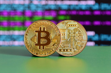 Two gold bitcoins lie on the green surface on the background of the display, which shows the...