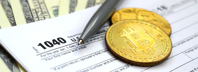 The pen, bitcoins and dollar bills is lies on the tax form 1040 U.S. Individual Income Tax Return....
