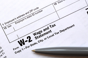 The pen lies on the tax form W-2 Wage and Tax Statement. The time to pay taxes
