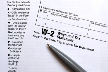 The pen lies on the tax form W-2 Wage and Tax Statement. The time to pay taxes