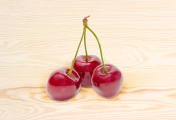 Three sweet cherries on stalks on a wooden surface