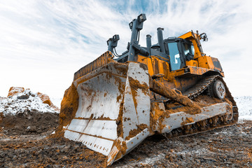 Yellow excavator in career moves overburden. Bulldozer combs the ground, with the bright sun and nice blue sky in the background - obrazy, fototapety, plakaty