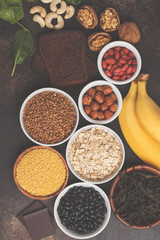 Healthy food nutrition dieting concept. Assortment of high magnesium sources. Banana chocolate spinach, buckwheat, nuts, beans, oat. Dark background