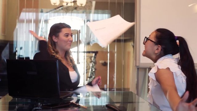 Two business women are happy to throw documents and clap their hands after one of them reported good news