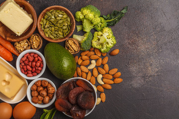 Healthy food nutrition dieting concept. Assortment of high vitamin A sources. Carrots, nuts, broccoli, butter, cheese, avocado, apricots, seeds, eggs. Dark background, copy space