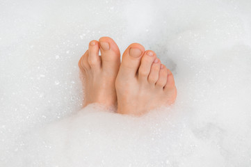 Beautiful female feet in bathtub with foam