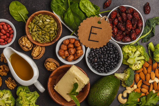 Healthy food nutrition dieting concept. Assortment of high vitamin E sources. Oil, nuts, avocado, butter, healthy fats, rose hips, parsley, seeds, spinach. Dark background, top view