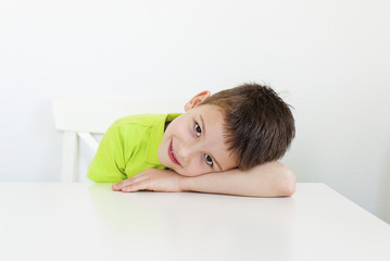 Closeup of adorable young boy on the table edge, smiling, head on hand.