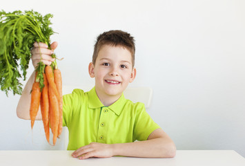 Closeup lovely young boy holds a carrot in his hand. White background.