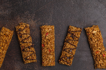 Granola bars and ingredients. Healthy sweet dessert snack. Cereal granola bar with nuts, chocolate  and berries on a dark background. Top view, copy space.