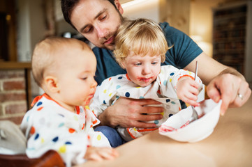 Father feeding two toddlers at home.