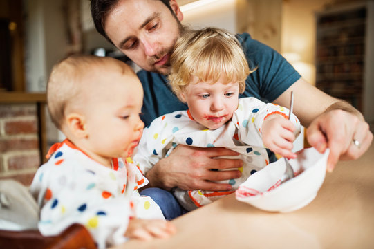 Father Feeding Two Toddlers At Home.