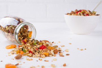 Fresh scattered granola from glass jar on white background. Copy space.