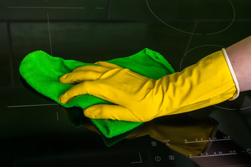 Hand in glove with green rag is wiping induction plates