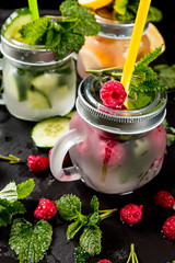 Home made mojito, Cucumber, lemon and raspberry fresh drink with fruits and vegetable on black background. 