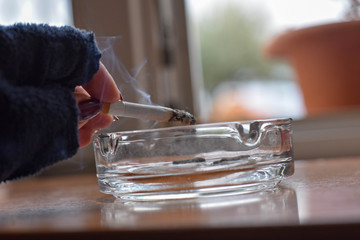 Woman hand holding cigarette whit smoke over ashtray/ Conceptual image of bad habit
