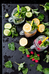 Mohito cucumber, lemon and raspberry drinks on black background. Fresh drinks with fruits on wood. Summer concept.