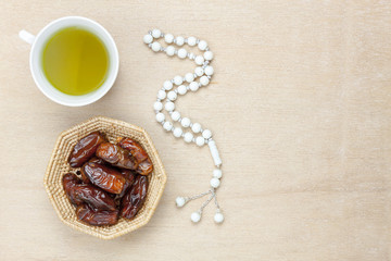 Table top view aerial image of decoration Ramadan Kareem holiday background.Flat lay date in wood basket with white rosary & green tea.Halal meal set for fasting is obligatory for Muslim on wooden.