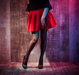 young woman legs in black stockings and red skirt on wooden background