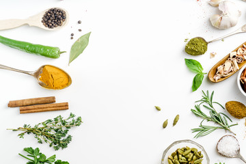 Fresh herbs and dried colorful spices in spoons and bowls arranged in frame on white background with copy space inside