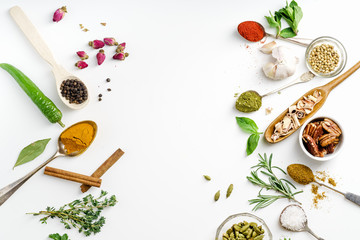 Fresh herbs and dried colorful spices in spoons and bowls arranged on one side with copy space