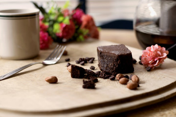piece of chocolate brownie on a wooden background with chocolate drops and nuts