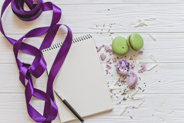 A flat lay of a macarons , notebook for records , the pen a white background