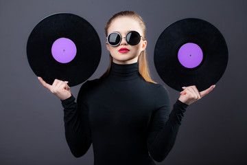 A beautiful girl holds vinyl records in her sunglasses. On a gray background