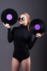 A beautiful girl holds vinyl records in her sunglasses. On a gray background