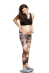 Unhappy pregnant woman standing on scales on white background