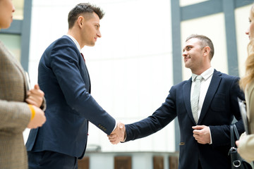 Content confident handsome young businessmen in formal suits making handshake after signing contract in office