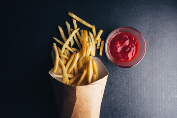 Top view of French fries with ketchup on black background.